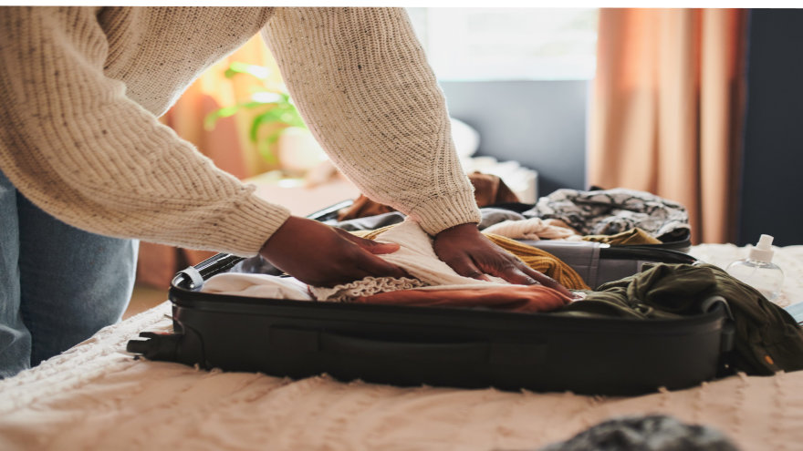 A woman packing her suitcase as it sits on her bed.