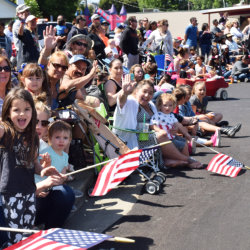 Group of community members waiving American flags and also waving at the camera during a Fiesta Days parade in Vacaville.
