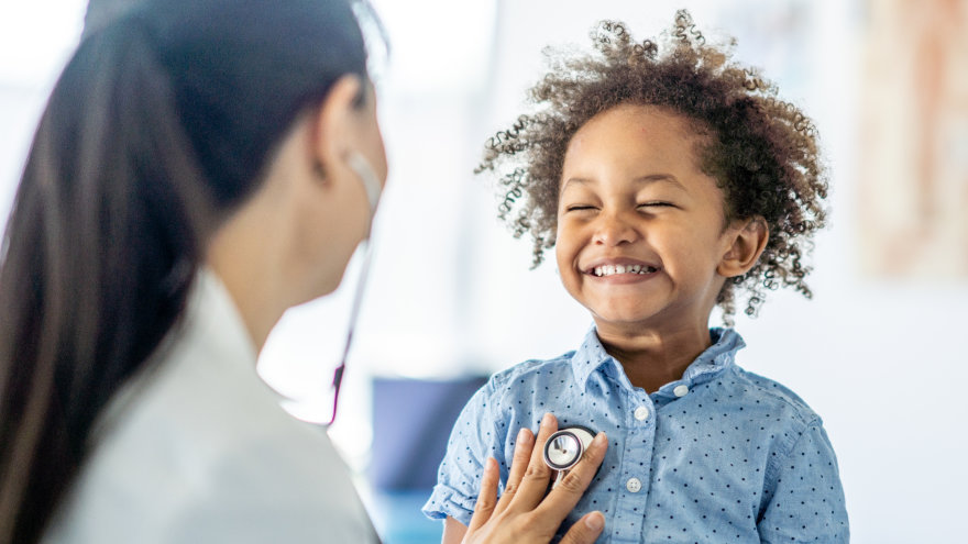 A provider placing her stethoscope on the chest of a smiling child.