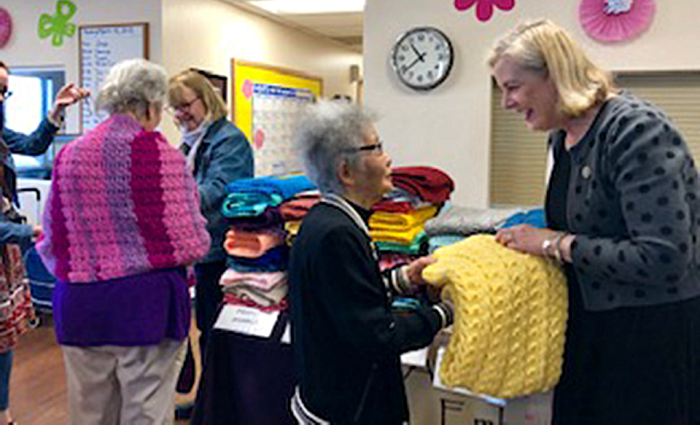 Diane Lewis of Alice’s Embrace, hands a blanket to an Adult Day Center program participant.