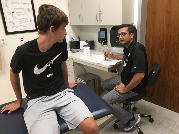 Orthopedic specialist Neil Pathare, M.D., chats with a student during a free physicals event. He will help run Saturday morning sports injury clinics this fall.